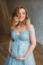 Young, pregnant woman posing in a luxurious, lush, blue dress The background is a light interior in Scandinavian style Royalty Free Stock Photo