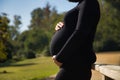 Young pregnant woman in profile in black dress, leaning on a wooden railing and holding her belly with her hands in the open air. Royalty Free Stock Photo