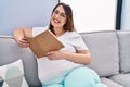 Young pregnant woman reading book sitting on sofa at home Royalty Free Stock Photo