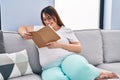 Young pregnant woman reading book sitting on sofa at home Royalty Free Stock Photo