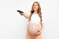 Pregnant woman with a remote control, on an isolated white background. Woman with tv controller switching tv channels Royalty Free Stock Photo