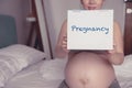 Young pregnant woman showing pregnancy message on white board on bed Royalty Free Stock Photo