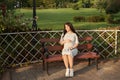 Young pregnant woman sitting on bench in park and holds sneakers for newborn Royalty Free Stock Photo