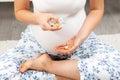 A young pregnant woman is sitting cross-legged on the floor with pills in her hands. Hands and medicine close-up. The Royalty Free Stock Photo