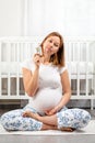 A young pregnant woman is sitting cross-legged on the floor, showing pills in her hands. The concept of health of Royalty Free Stock Photo