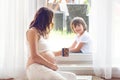 Young pregnant woman, sitting indoor, watching her child through