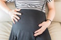 Young pregnant woman sitting on sofa putting hands on belly