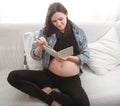 Young pregnant woman sitting on the sofa and reading a book Royalty Free Stock Photo