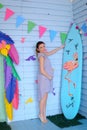 Young pregnant woman standing near surfboard and decorated children house.