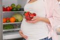 Young pregnant woman with strawberries near fridge at home, closeup. Healthy eating Royalty Free Stock Photo