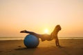 Young pregnant woman stretching on training ball against sunset over sea. Beauty and health during pregnancy. Yoga, Pilates