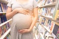 Young pregnant woman touching her belly in bookstore.