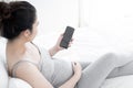 Young pregnant woman using smartphone with blank screen lying on bed. Royalty Free Stock Photo