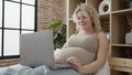 Young pregnant woman watching video on laptop lying on bed at bedroom Royalty Free Stock Photo