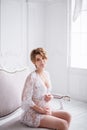 Young pregnant woman wearing lace dress in white interior. Fashion shot. Royalty Free Stock Photo