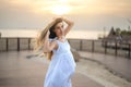 Young pregnant woman in a white dress enjoying the breeze on the beach promenade near the ocean coastline at sunset. Royalty Free Stock Photo