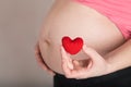 Young pregnant woman keeps small red plush heart close to her belly Royalty Free Stock Photo