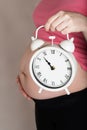 Young pregnant woman keeps vintage alarm clock close to her belly Royalty Free Stock Photo