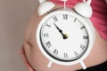 Young pregnant woman keeps vintage alarm clock close to her belly Royalty Free Stock Photo