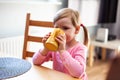 Young preschool girl with ponytails standing near a table, child drinking from a yellow cup / mug by herself, drinking