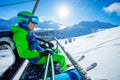 Boy sit in helmet, mask with ski on chairlift over mountains Royalty Free Stock Photo