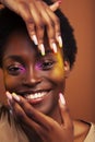 Young pretty african girl with bright colorful makeup and manicure posing cheeful on brown background, lifestyle people Royalty Free Stock Photo