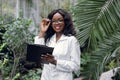 young pretty african woman botanist scientist, working in green house with tropical plants and palm trees. Smiling Royalty Free Stock Photo