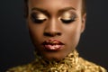 Young pretty african woman, with hair gathered in hairstyle and sensitive gold make-up, posing on black background, in studio, clo