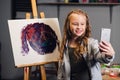 A young pretty artist takes a selfie against the background of her painting in the Studio.