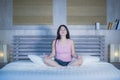 Young pretty Asian Chinese woman 20s or 30s relaxing at home bedroom sitting on bed in lotus yoga position in meditation and relax Royalty Free Stock Photo