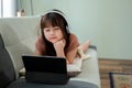 Young pretty Asian girl is studying online on her digital tablet while lying on a sofa Royalty Free Stock Photo