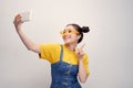 Young pretty Asian girl who wearing a jeans dungaree and yellow glasses, taking selfie, smiling