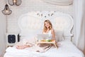 Young pretty blond woman sitting on bed with laptop having breakfast, freelancer or blogger at home. Woman works on Royalty Free Stock Photo