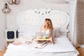 Young pretty blond woman sitting on bed with laptop having breakfast, freelancer or blogger at home. Woman works on Royalty Free Stock Photo