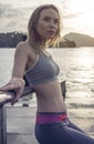 Young pretty blonde female wearing exercise clothing standing on the pier near the sea and enjoying early morning with beautiful Royalty Free Stock Photo