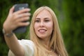 Young beautiful blonde girl in a dress makes a selfie on the street in summer.