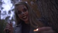 Young pretty blonde girl with horrifying Halloween make-up holding hatchet and small candle in hands. Caucasian woman