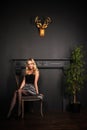 Young pretty blonde girl is sitting on the chair in evening shiny dress close up on the grey wall background in the photo studio Royalty Free Stock Photo