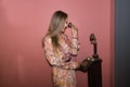 Young, pretty, blonde woman in a flowered dress dialing on the dial of an antique candlestick telephone on a magenta background. Royalty Free Stock Photo