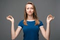 Pretty blonde woman meditates, holds fingers in yoga sign. Relaxation concept. Studio shot gray background