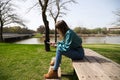 A young, pretty, blonde woman is sitting at a wooden table in the park, looking at her mobile phone and smoking a cigarette. In Royalty Free Stock Photo