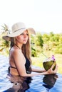 Young pretty blonde woman in swimming pool with coconut coctail