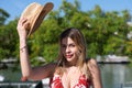 Young, pretty blonde woman takes straw hat off her head. She is dressed in a white dress with red print and is having fun doing Royalty Free Stock Photo