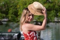 Young, pretty blonde woman takes straw hat off her head. She is dressed in a white dress with red print and is having fun doing Royalty Free Stock Photo