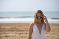 Young, pretty, blonde woman in a white dress, looking flirtatiously over sunglasses, on the beach. Concept sunglasses, beach, Royalty Free Stock Photo