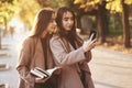 Young pretty brunette twin girls looking at each other and taking selfie with black phone, while one of them is holding Royalty Free Stock Photo