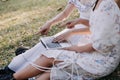 Young pretty brunette twin girls sitting on the grass with legs slightly bent in knees and looking in a brown book, wearing casual Royalty Free Stock Photo