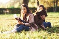 Young pretty brunette twin sisters sitting back to back on the grass with legs slightly bent in knees with brown books Royalty Free Stock Photo