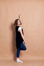 Young pretty brunette woman with curly hair, standing by wall, posing, wearing white top, black vest and blue jeans. A portrait of Royalty Free Stock Photo