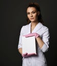 Young pretty brunette woman doctor therapist nurse in white uniform and protective gloves holding blank paper sheet